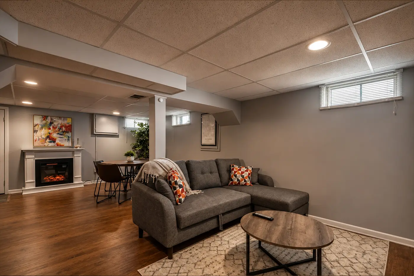 Finished basement living space with a gray sectional sofa, fireplace, and dining nook