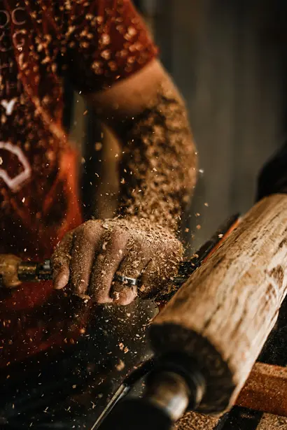 Close-up of a craftsman shaping wood on a lathe, sawdust in motion